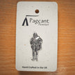 A silver pewter pin of a William Shakespeare, mounted on a speckled white display card from the brand Pageant Pewter, placed on a wooden surface.