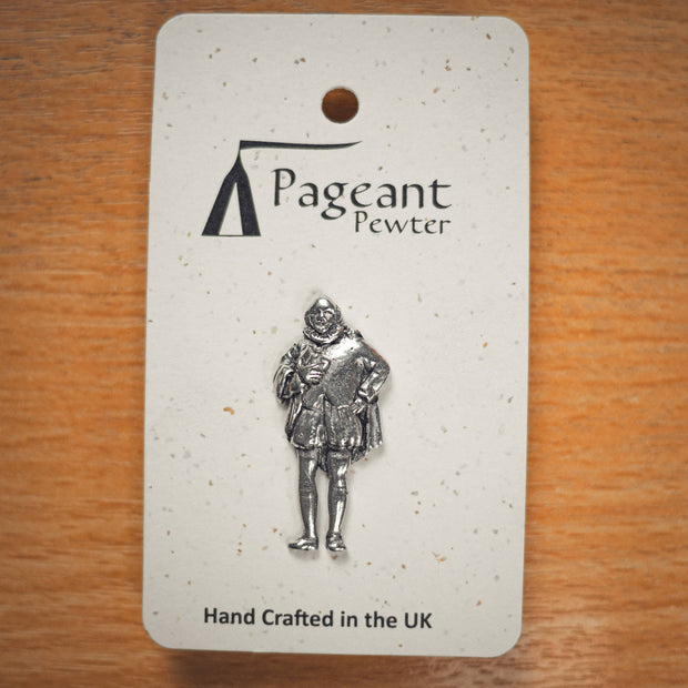 A silver pewter pin of a William Shakespeare, mounted on a speckled white display card from the brand Pageant Pewter, placed on a wooden surface.