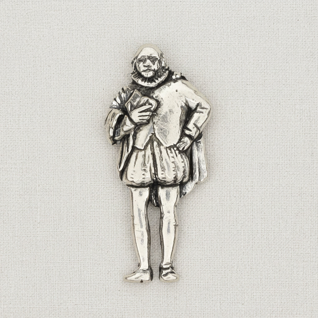 A pewter metal pin depicting a William Shakespeare in a ruff collar and knee-length tunic, shown on al ight textured fabric background.
