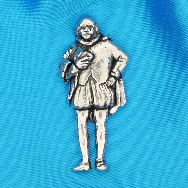 A pewter metal pin depicting a William Shakespeare in a ruff collar and knee-length tunic, shown on a bright blue textured fabric background.
